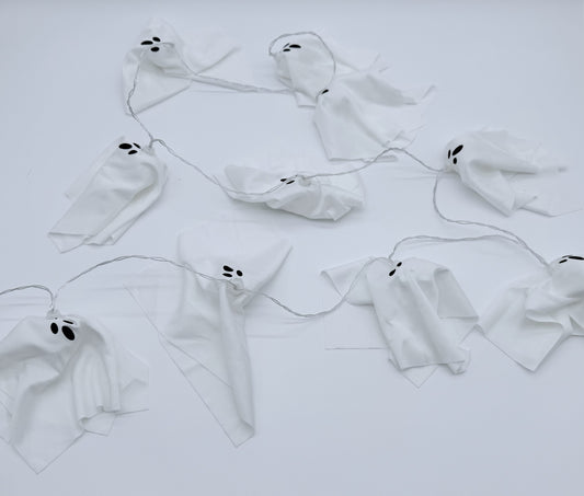 White ghost garland with black embroidered eyes and mouths, strung along a thin wire against a plain white background.