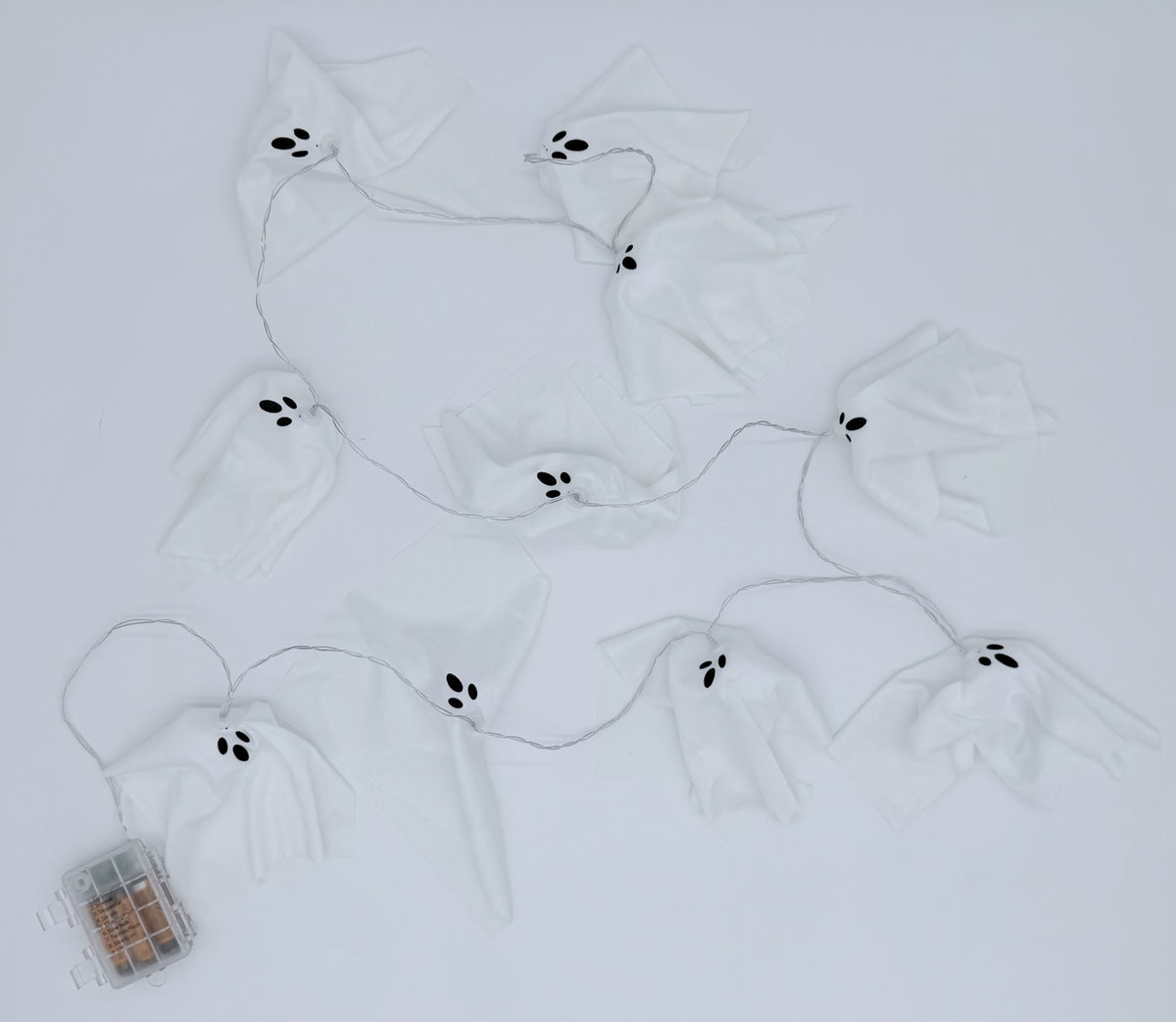 White ghost-shaped string lights with black embroidered eyes and mouths, arranged on a white background with a small battery compartment visible in the lower left corner.